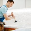 Male plumber in uniform holds plunger, problem with clog in the kitchen. Handyman with toolbag repair sink, sanitary equipment service at home